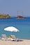 White sunshade with two chairs on a sandy beach with ship anchored by the old roman fortress in a background, Sithonia