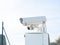 White surveillance camera on a stand outdoors behind a fence