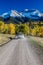 White SUV drivews down Country Road 12 out of Ridgway Colorado towards San Juan Mountains with Autumn Color