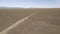 A white SUV is driving fast on a dusty road. Drone