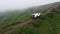 White SUV rides on a mountainous terrain on a dirt road in the cloud. Aerial view.