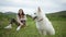 White swiss shepherd dog and its young woman owner sitting on the outdoor lawn.