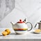 A white table with a Bauhaus teapot rests against a traditional kitchen backdrop