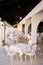 White tables with tablecloths and chairs stand on the covered veranda of the restaurant with columns