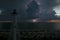 White tall lighthouse on sea shore with blinking light at stormy night for commercial vessels navigation. Thunderstorm