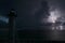 White tall lighthouse on sea shore with blinking light at stormy night for commercial vessels navigation. Thunderstorm