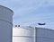 White tanks in tank farm with blue sky and approaching aircraft