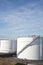 White tanks in tank farm with blue sky and approaching aircraft