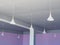 White tapeths of conical shape hang on the ceiling with a beam in the middle and light lilac walls around