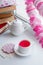 A white tea cup with pink scented tea and saucer sits on a white background with colourful paper bunting and interior details,