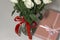 White tea roses stand in a glass vase, which is tied with a red ribbon and stands on the table. There is a gift nearby. in a pink