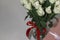 White tea roses stand in a glass vase, which is tied with a red ribbon and stands on the table. There is a gift nearby. in a pink