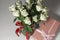 White tea roses stand in a glass vase, which is tied with a red ribbon and stands on the table. There is a gift nearby. in a pink