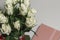 White tea roses stand in a glass vase, which is tied with a red ribbon and stands on the table. There is a gift nearby. in a pink