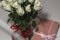 White tea roses stand in a glass vase, which is tied with a red ribbon and stands on the table. There is a gift nearby. in a pink