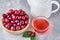 White teapot, herbal tea in glass cup and fresh cherry in wooden bowl on a gray background