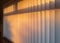 White textured vertical slat blinds hanging in front of a window as the sun is setting turning the light golden.