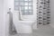 White toilet bowl, stainless steel bidet spray and glass block in partition wall with tile wall decoration inside of modern