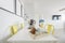 White toned dining table with yellow chairs, dried flower arrangement and wooden tray with bowls and glasses