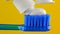 white toothpaste is placed on a blue toothbrush on a yellow background close-up.