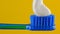 White toothpaste is placed on a blue toothbrush on a yellow background in close-up. Poor quality product