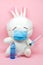 White toy bunny in medical mask with an ampoule and syringe on pink background. space for text. Children\\\'s vaccination