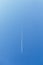 White trace of smoke from flying airplane. Vertical image. Plane flying in blue sky and living white track line smoke. Aircraft