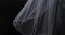 A white translucent veil blowing in the wind. Wedding veil on a dark background.