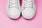 White trendy sneakers on pink pastel background. Front view