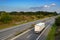 White truck is driving on the highway through the country landscape under a blue sky with clouds, transport and environment