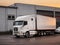 white truck parked in front of industrial logistics building at sunset. Logistics transport trucks are parked