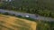 White truck rides on the highway among a dense forest. Traveling on the forest asphalt road aerial footage. Highway