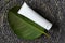 White tube for cream, moisturizer, lotion, facial cleanser or shampoo on raffia weave background and green tropical leaf. Natural