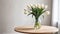 White tulips in paunchy vase on round wooden brown table against empty gray wall. Minimalistic interior. Scandinavian style