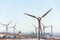 White turbines at wind farm with power station and sea in background, arid landscape on sunny summer day