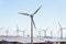 White turbines at wind farm with power station and sea in background, arid landscape on sunny summer day