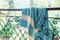 A white and turquoise Turkish peshtemal / towel on a wrought iron railings with blurry nature in the background.