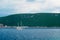 White two-masted schooner sails along the rocky coast against the backdrop of mountains