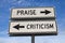 White two street signs with arrow on metal pole with word Praise and Criticism