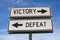 White two street signs with arrow on metal pole with word victory and defeat