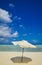 White umbrella on idyllic tropical sand beach. White beach umbrella and blue sky. Sun and umbrella on the beach. Summer beach