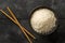 White uncooked, raw long grain rice in black bowl on rustic, dark wooden table top view flat lay from above