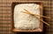 White uncooked, raw long grain rice on wooden plate with chopsticks on bamboo mat with copy space top view flat lay from above