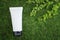 White unlabelled cosmetic bottle, on a green natural background, grass, moss with branches of greenery. Eco friendly cosmetology