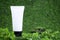 White unlabelled cosmetic bottle, on a green natural background, grass, moss with branches of greenery. Eco friendly cosmetology