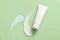 A white, unmarked cosmetic tube adorned with streaks of cosmetics on a light green background.