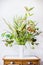 White vase with bunch of various green plant on table. Florist arrangements with variety of green tropical plants. Home decor with