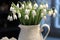 A white vase filled with white flowers on top of a table, early spring flowers, snowdrops.