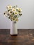 White vase full of fresh cut daisy flowers sitting on a wooden cutting board with a white wall behind.  A little outdoor nature
