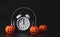 White vintage alarm clock show 12 o`clock cover with headphones with halloween pumpkins on black background. Scary story or